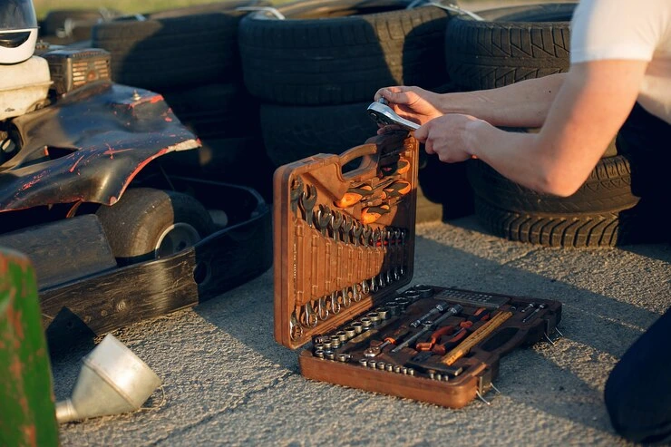 Person using a roadside tool kit to repair a vehicle tyre with spare tyres in the background